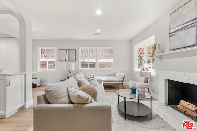 living room featuring a brick fireplace, light hardwood / wood-style floors, and a healthy amount of sunlight