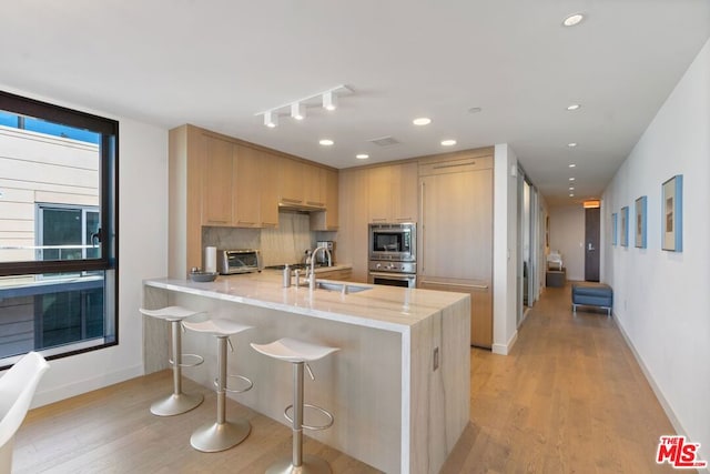 kitchen featuring sink, stainless steel appliances, light stone counters, kitchen peninsula, and light brown cabinets