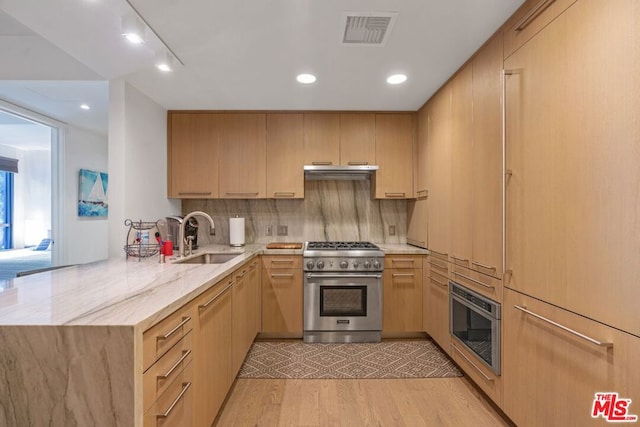 kitchen with sink, high end stove, light hardwood / wood-style floors, light brown cabinetry, and kitchen peninsula