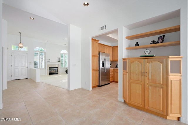 kitchen featuring stainless steel refrigerator with ice dispenser, light tile patterned floors, hanging light fixtures, and light brown cabinets