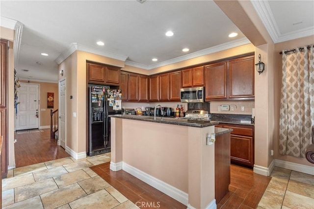 kitchen featuring light tile patterned flooring, appliances with stainless steel finishes, dark stone counters, ornamental molding, and a center island with sink