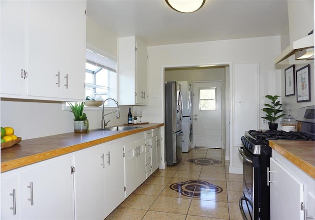 kitchen with stainless steel refrigerator, sink, white cabinets, gas range, and wall chimney exhaust hood