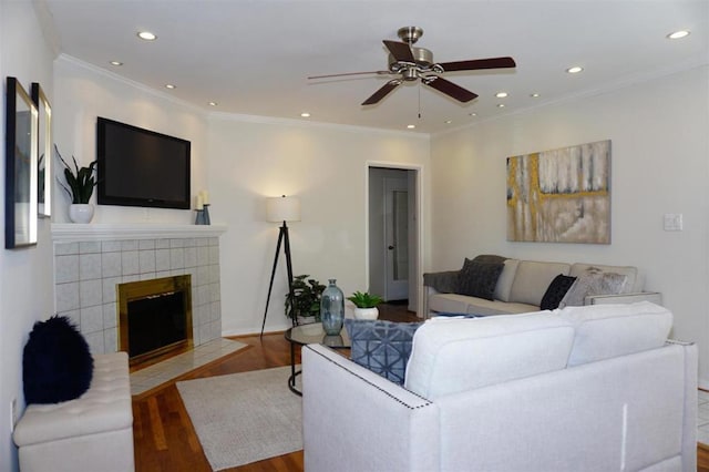 living room with hardwood / wood-style flooring, ceiling fan, ornamental molding, and a tile fireplace