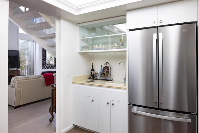 bar featuring stainless steel fridge, light hardwood / wood-style floors, sink, and white cabinets