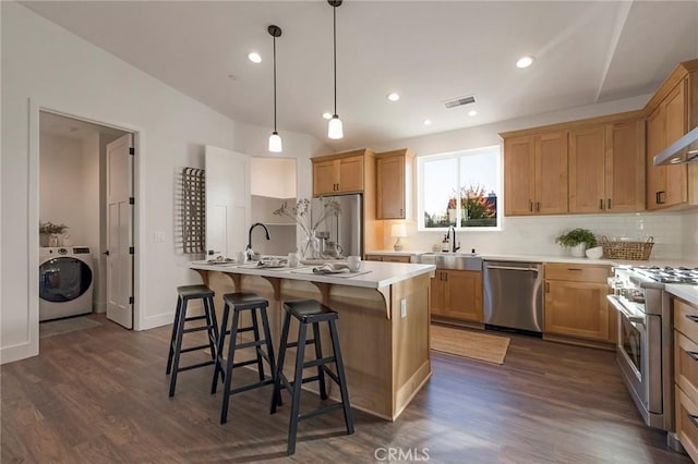 kitchen with pendant lighting, tasteful backsplash, washer / dryer, high end appliances, and a center island with sink