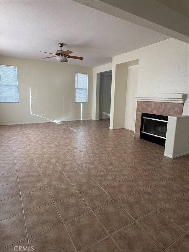 unfurnished living room featuring ceiling fan, a tiled fireplace, dark tile patterned flooring, and a wealth of natural light