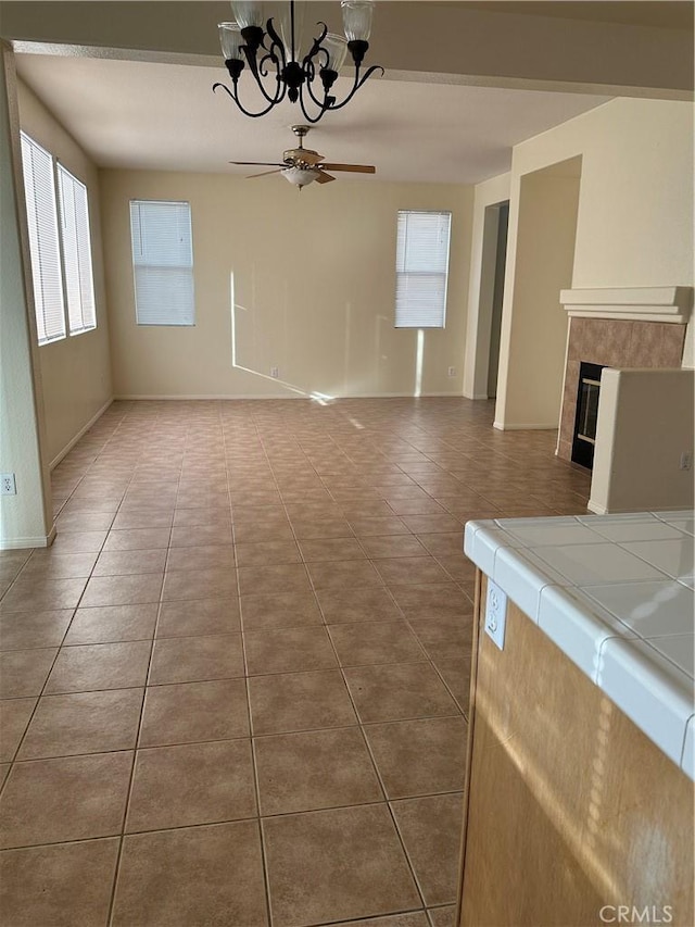 unfurnished living room with ceiling fan with notable chandelier, a fireplace, and tile patterned floors