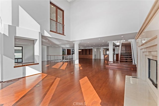 unfurnished living room featuring decorative columns, a premium fireplace, hardwood / wood-style flooring, and a high ceiling