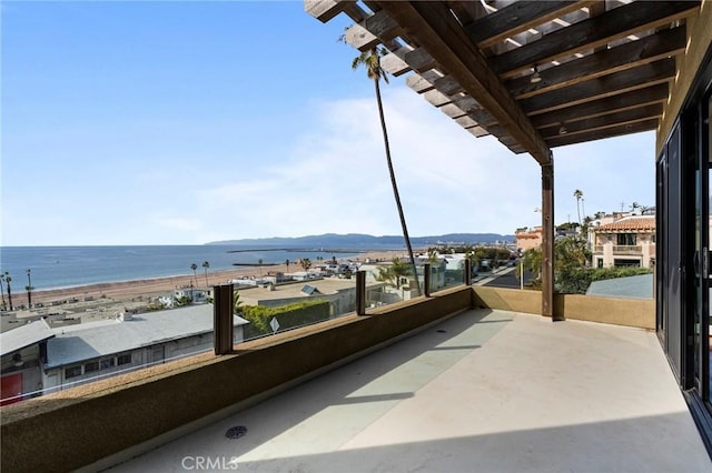 balcony with a view of the beach, a water view, and a pergola