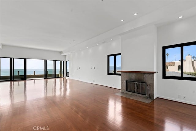 unfurnished living room with a water view, plenty of natural light, hardwood / wood-style floors, and a fireplace