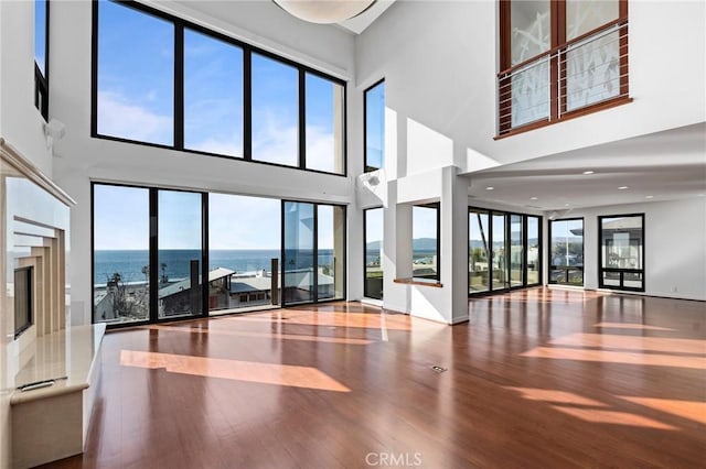 interior space featuring a towering ceiling, wood-type flooring, and a water view