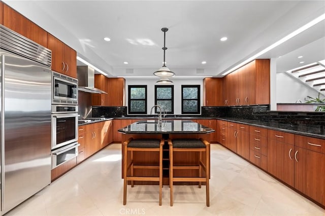 kitchen featuring pendant lighting, dark stone countertops, a kitchen breakfast bar, built in appliances, and an island with sink