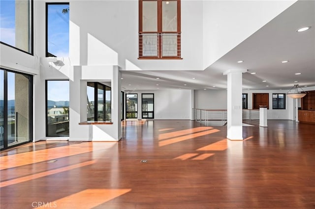 unfurnished living room featuring hardwood / wood-style flooring, a towering ceiling, and ornate columns