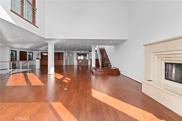 unfurnished living room with ornate columns, wood-type flooring, a towering ceiling, and a high end fireplace