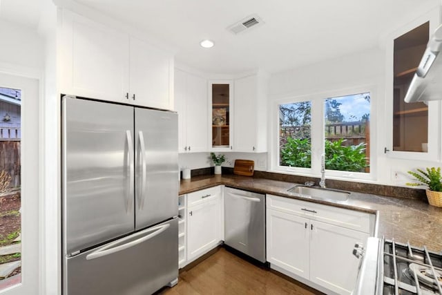 kitchen featuring appliances with stainless steel finishes, range hood, white cabinetry, sink, and dark hardwood / wood-style flooring