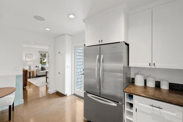 kitchen featuring white cabinetry, stainless steel fridge, light hardwood / wood-style floors, and dark stone countertops