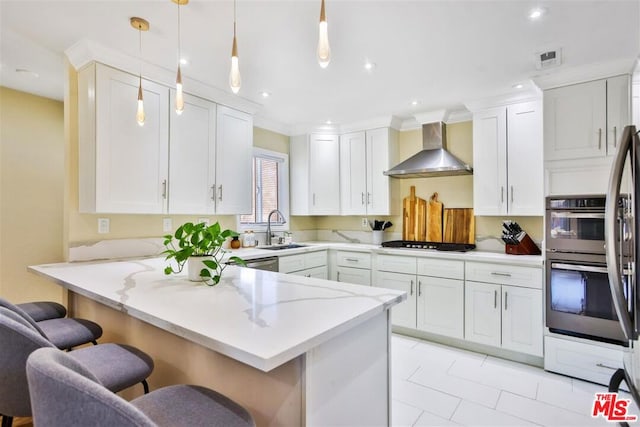 kitchen featuring pendant lighting, wall chimney range hood, sink, a kitchen breakfast bar, and kitchen peninsula