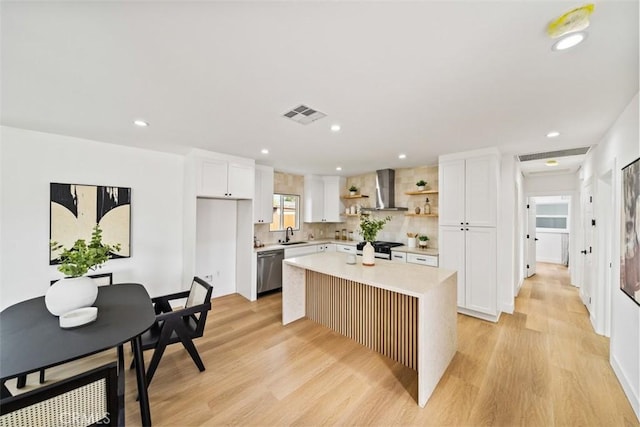 kitchen with open shelves, light countertops, stainless steel dishwasher, light wood-style floors, and wall chimney range hood