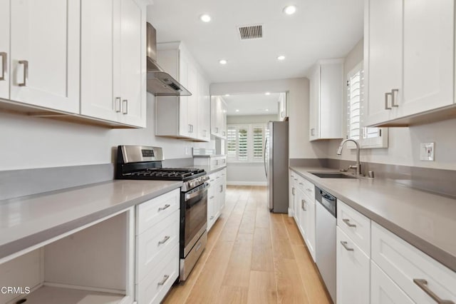 kitchen with white cabinetry, wall chimney range hood, stainless steel appliances, and sink