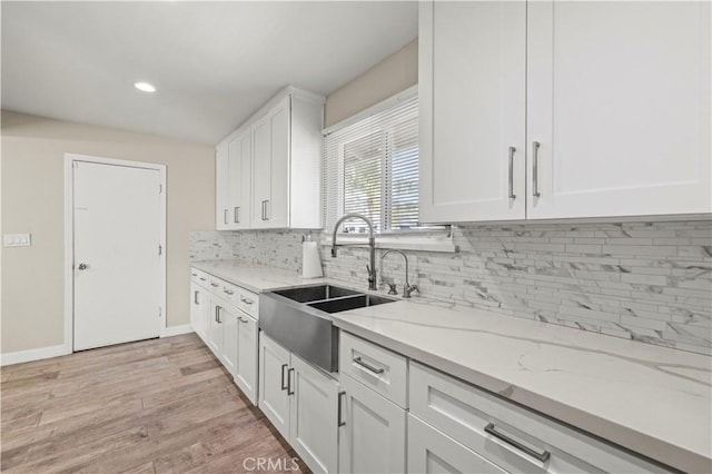 kitchen featuring white cabinetry, sink, decorative backsplash, light stone counters, and light wood-type flooring