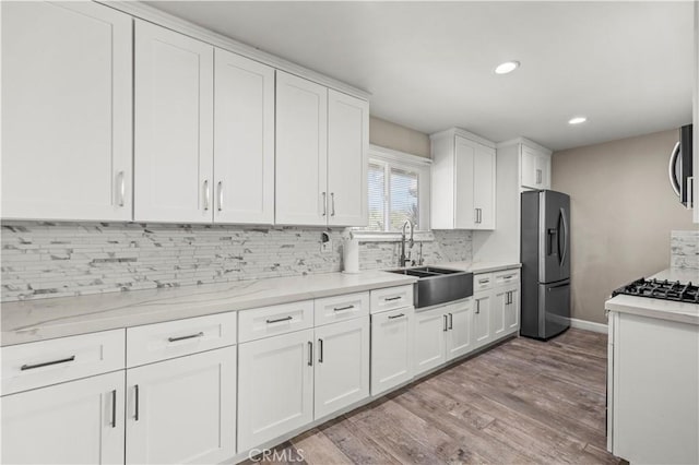 kitchen featuring sink, appliances with stainless steel finishes, white cabinetry, backsplash, and light wood-type flooring