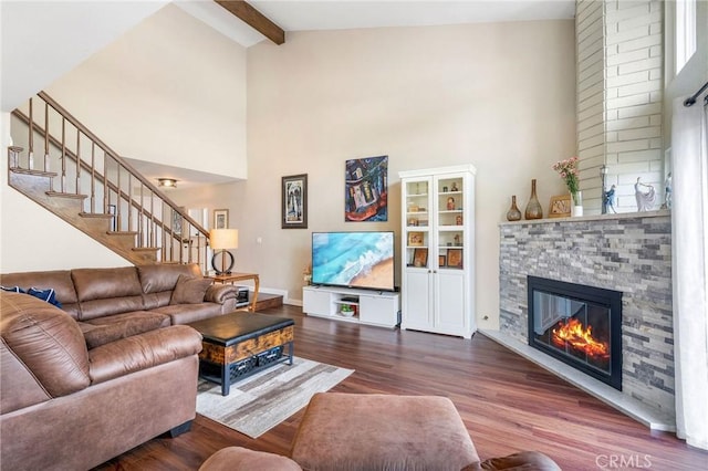 living room featuring beam ceiling, hardwood / wood-style flooring, a stone fireplace, and high vaulted ceiling