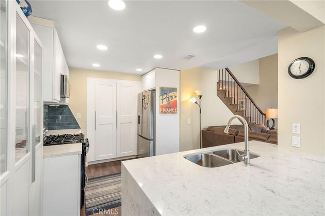 kitchen with sink, white cabinets, stainless steel fridge with ice dispenser, gas stove, and light stone countertops