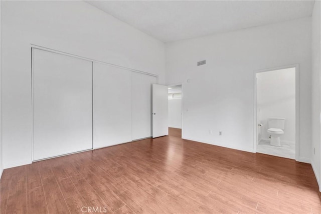 unfurnished bedroom featuring ensuite bathroom, hardwood / wood-style floors, high vaulted ceiling, and a closet