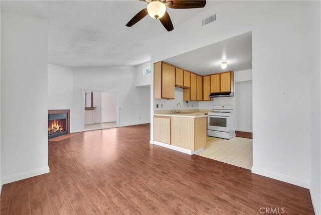 kitchen with sink, light brown cabinetry, gas range gas stove, a tiled fireplace, and light wood-type flooring