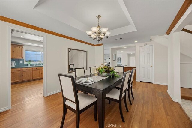 dining room featuring sink, a raised ceiling, a chandelier, and light wood-type flooring