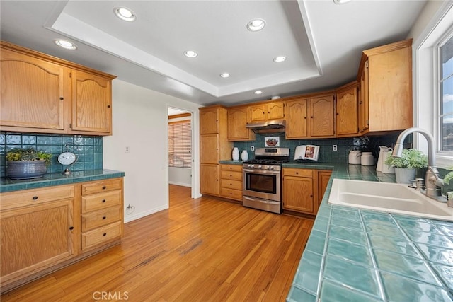 kitchen featuring stainless steel range with gas cooktop, tile countertops, a raised ceiling, and sink