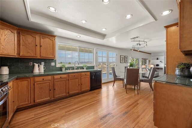 kitchen with tasteful backsplash, dishwasher, sink, a raised ceiling, and light wood-type flooring