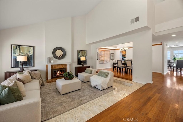 living room featuring an inviting chandelier, a towering ceiling, a premium fireplace, and light hardwood / wood-style flooring