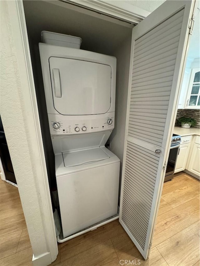 laundry area featuring stacked washer / drying machine and light wood-type flooring