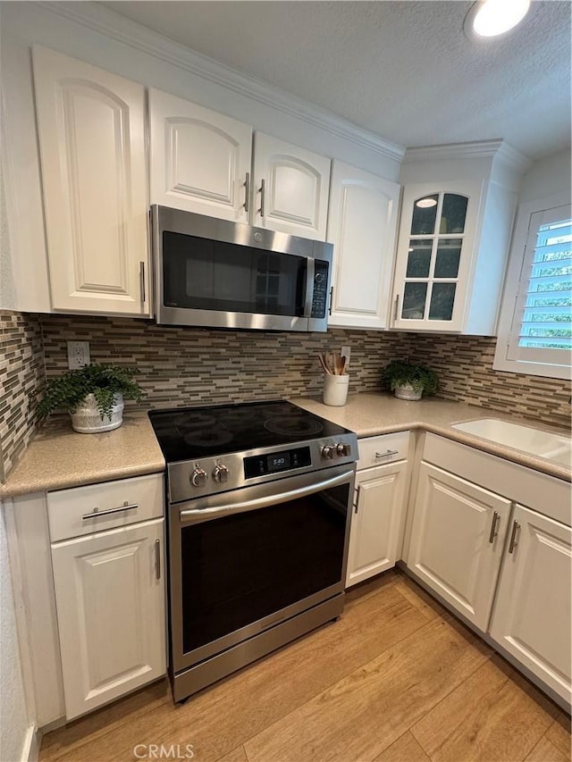 kitchen with sink, light hardwood / wood-style flooring, white cabinetry, backsplash, and stainless steel appliances