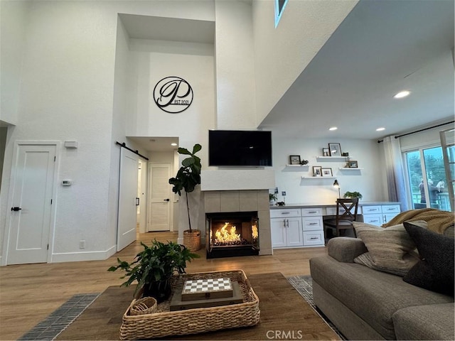 living room featuring built in desk, a high ceiling, a tile fireplace, and light wood-type flooring