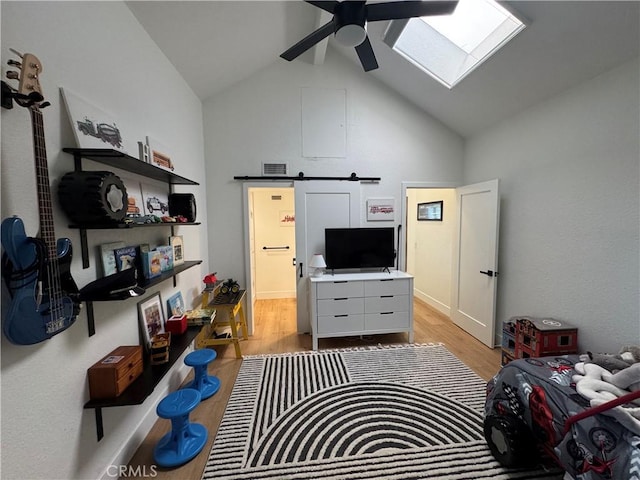 living room featuring light hardwood / wood-style flooring, ceiling fan, a skylight, high vaulted ceiling, and a barn door