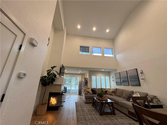 living room with a tiled fireplace, wood-type flooring, and a high ceiling