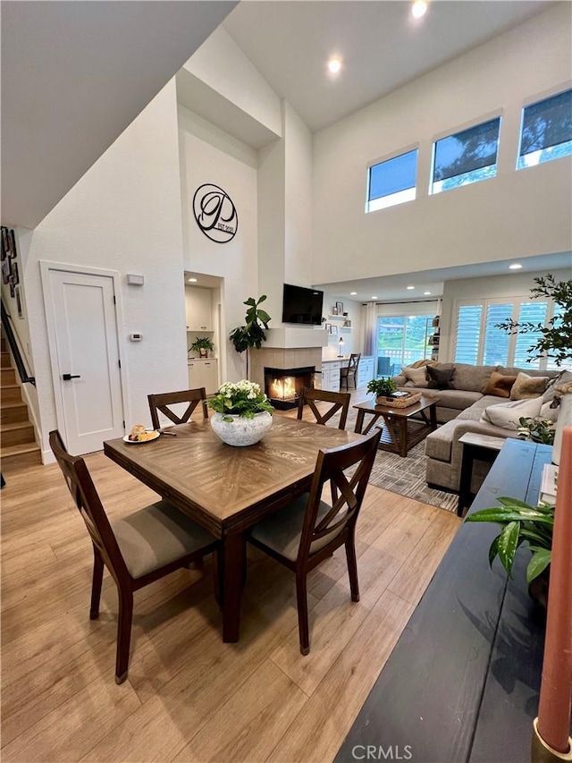 dining area featuring a towering ceiling, a fireplace, and light hardwood / wood-style floors