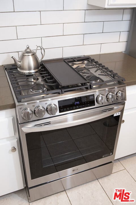 interior space featuring decorative backsplash, stainless steel gas range oven, and white cabinets