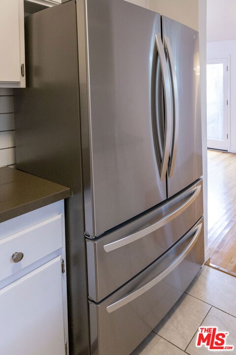 kitchen with light tile patterned flooring, stainless steel fridge, and white cabinets