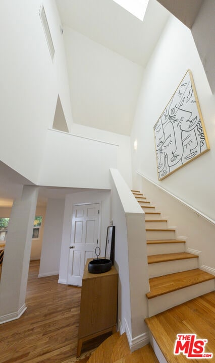 stairway featuring wood-type flooring, a skylight, and high vaulted ceiling