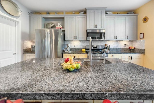 kitchen featuring stainless steel appliances, sink, decorative backsplash, and dark stone countertops