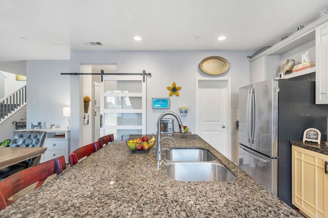 kitchen with sink, a breakfast bar area, stainless steel refrigerator, a barn door, and white cabinets