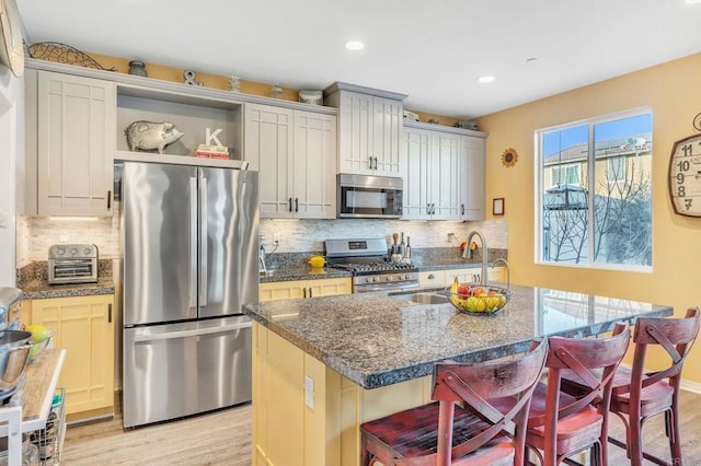 kitchen featuring stainless steel appliances, a kitchen bar, an island with sink, and stone counters