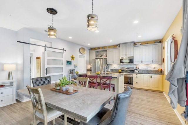 dining space with a barn door, sink, and light wood-type flooring