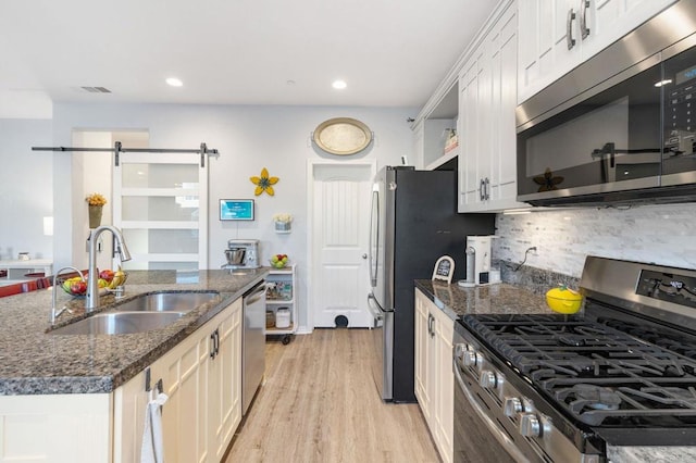 kitchen with white cabinetry, sink, a barn door, and appliances with stainless steel finishes