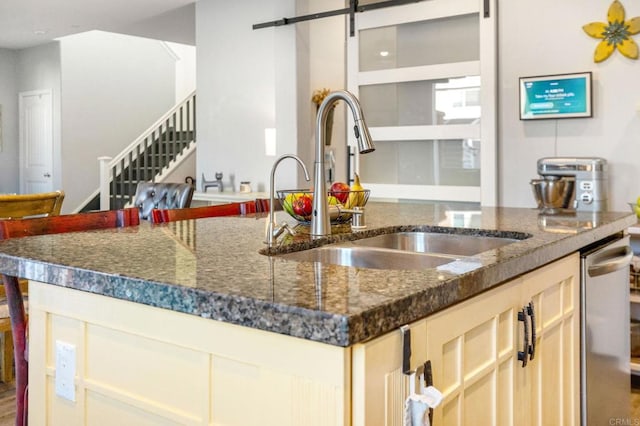 kitchen featuring light brown cabinetry, sink, dishwasher, dark stone counters, and a barn door