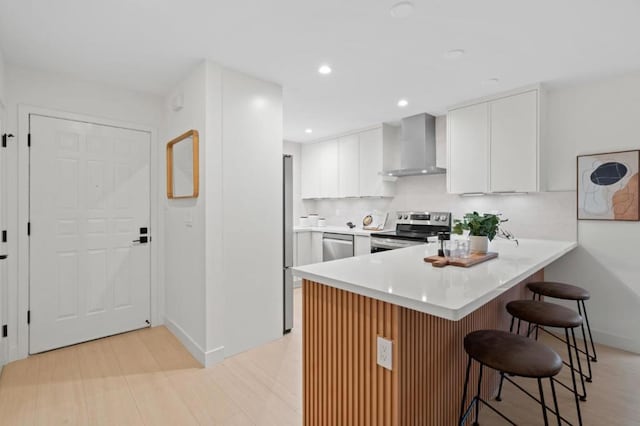 kitchen featuring appliances with stainless steel finishes, a breakfast bar, white cabinetry, kitchen peninsula, and wall chimney exhaust hood