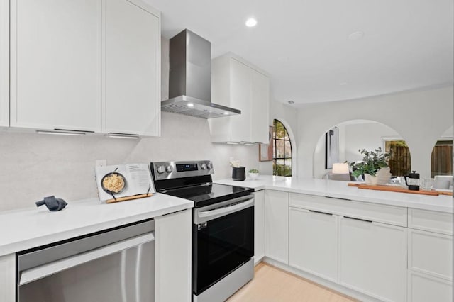 kitchen with appliances with stainless steel finishes, wall chimney exhaust hood, light wood-type flooring, and white cabinets